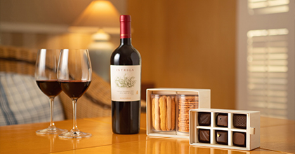 Image of a table with two wine glasses filled with wine, one bottle of house wine, two types of cookies, and six pieces of chocolate.